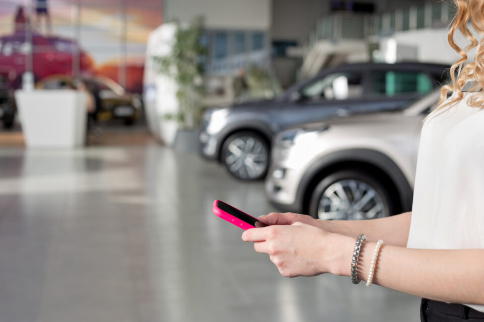 Woman dealer using mobile smart phone at dealer showroom. Modern working process.