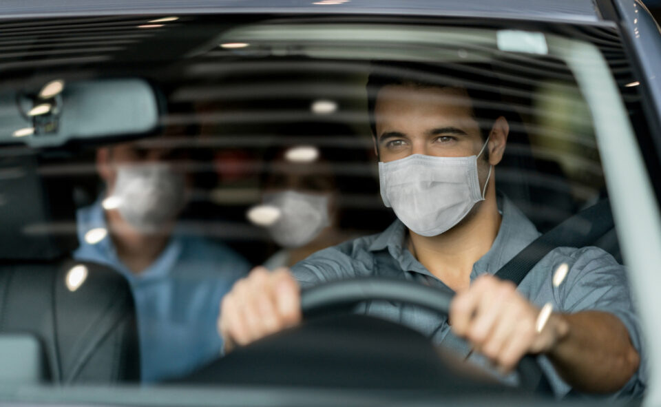 Portrait of a crowdsource taxi driver wearing a facemask while driving a couple of customers during the COVID-19 pandemic
