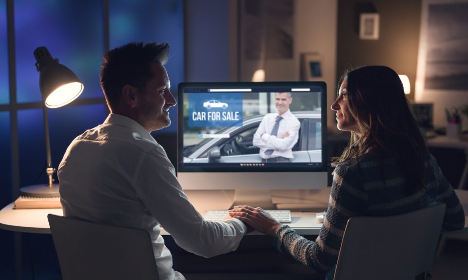 Young smiling couple holding hands and connecting with a computer late at night, they are buying a car online